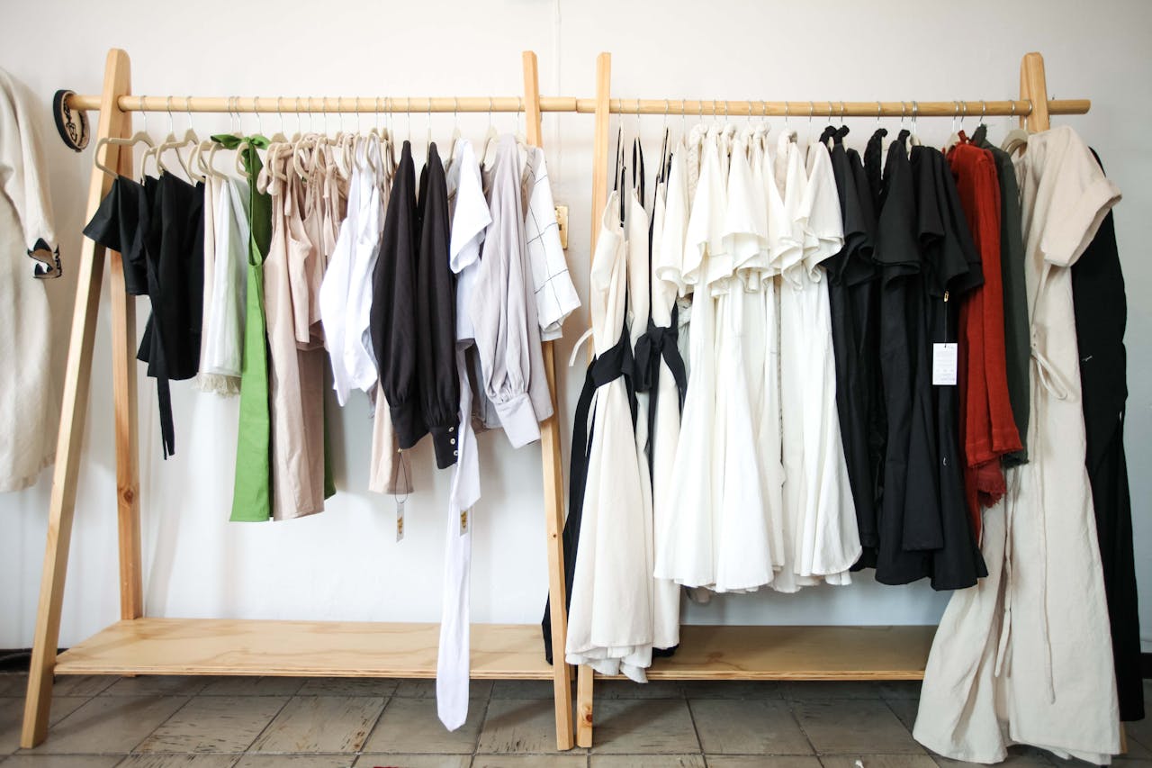 A variety of stylish clothes hanging on a wooden clothing rack indoors.