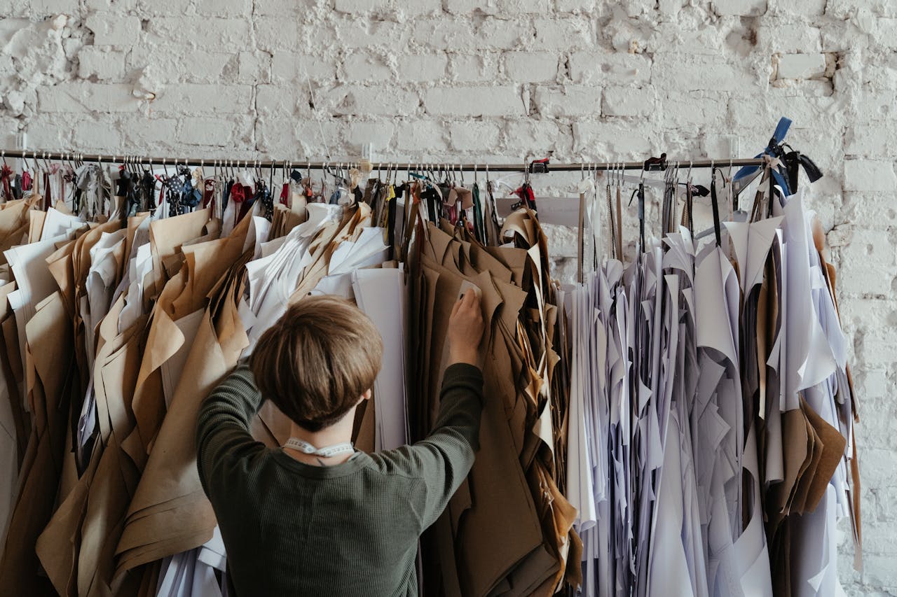 Back view of designer organizing sewing patterns against a rustic wall.